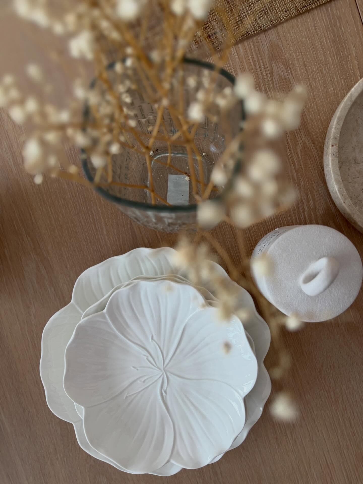 Stack of white floral plates with a small white lidded jar and dried flowers.
