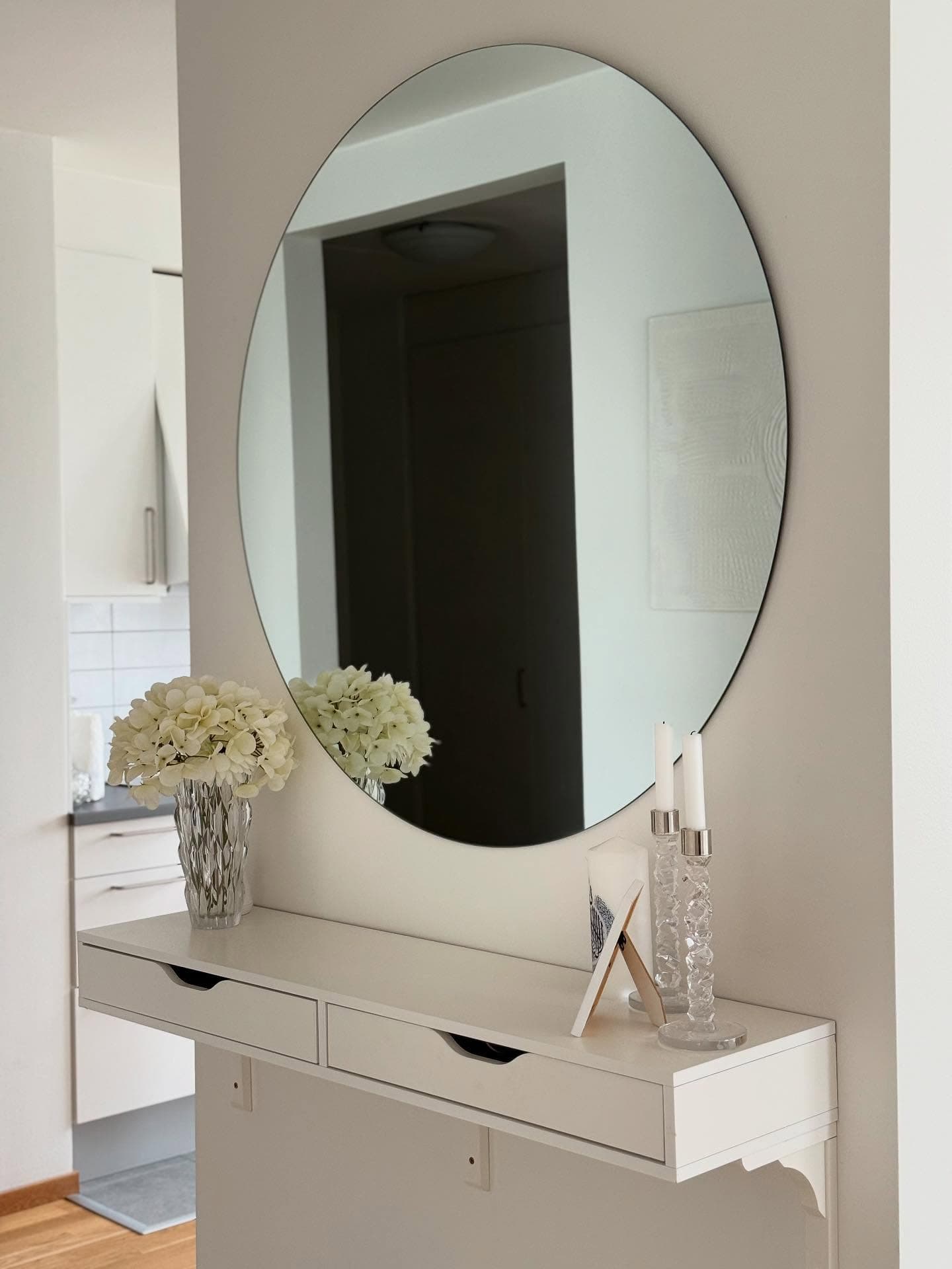 Interior with round mirror above white floating console table. Flowers, candles, and picture frame decorate the surface.