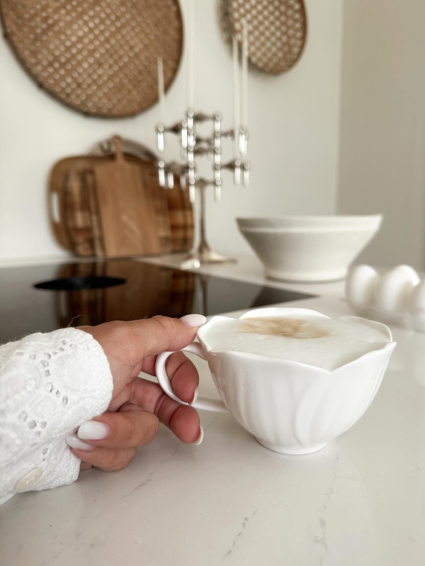 Close-up of hand holding white teacup with latte on marble countertop.
