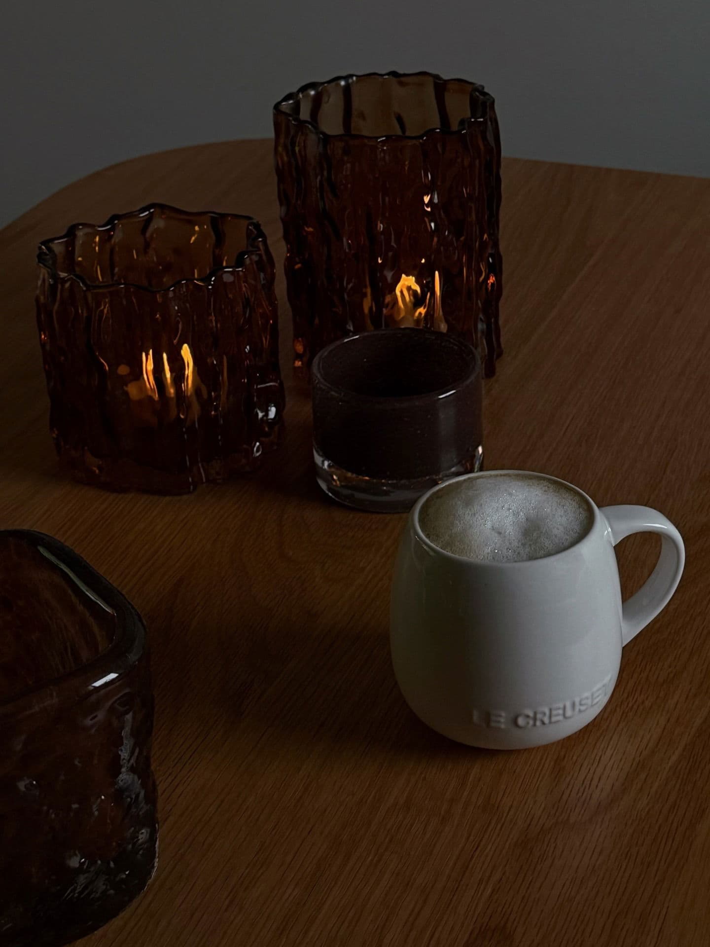 Still life featuring Le Creuset mug, brown glass candle holders, and moody lighting.
