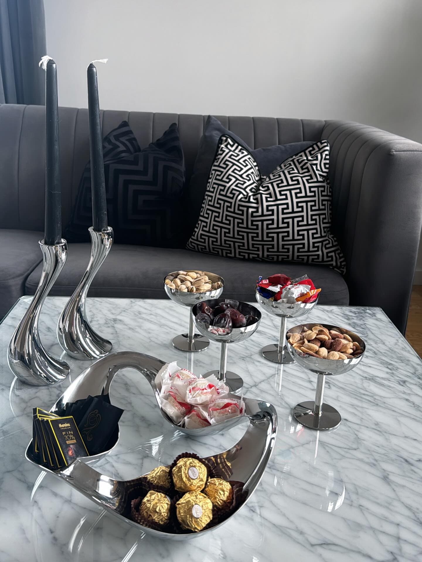 Living room scene with snacks, candles, and decorative pillows on a gray couch.